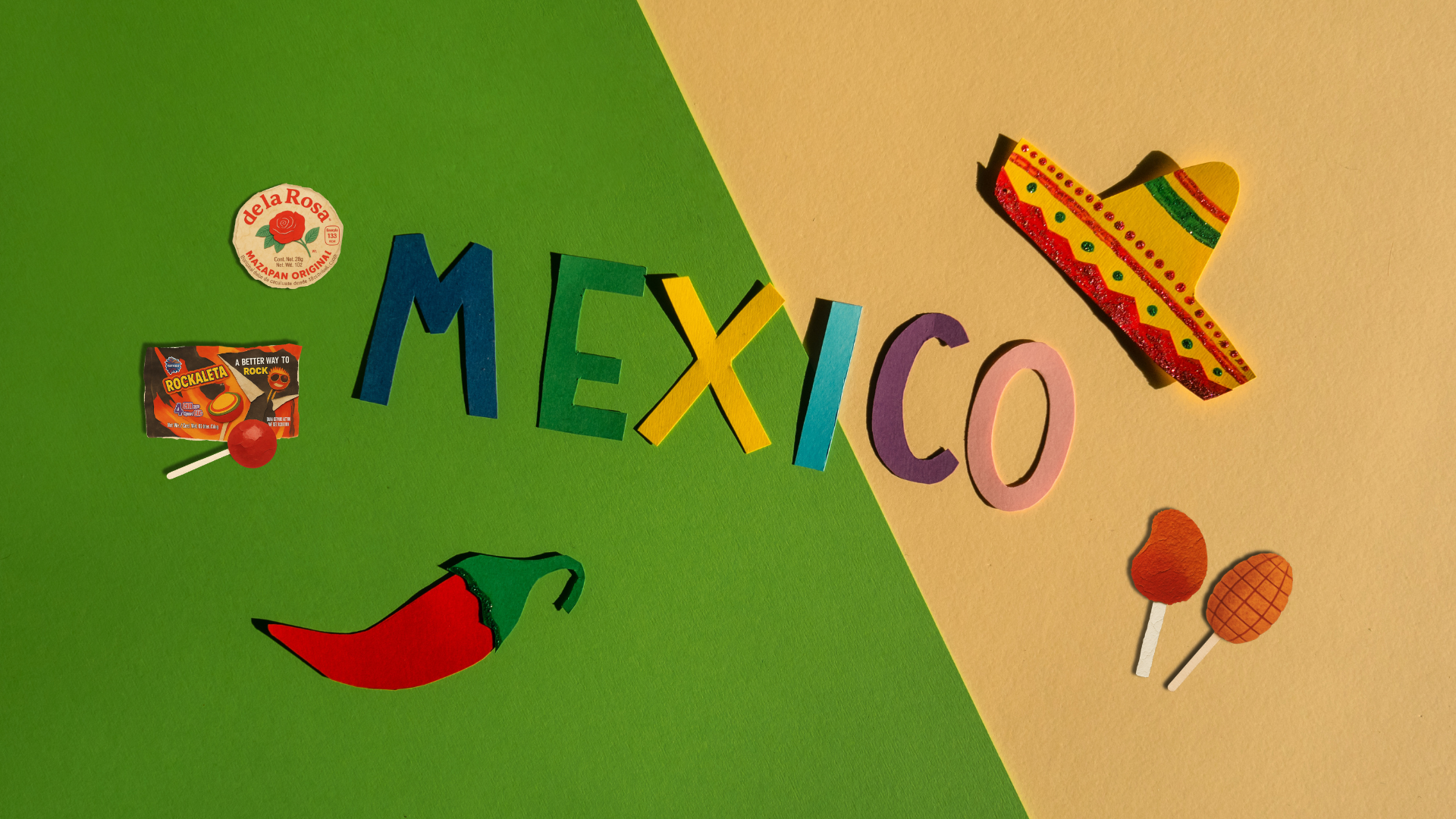 A flat-lay arrangement spelling out 'MEXICO' with colorful cutout letters and Mexican-themed props, including a sombrero, chili pepper, mexican lollipops, and a mazapan, on a split green and beige background.